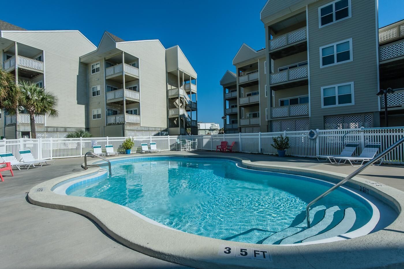 A swimming pool with a 3.5 ft depth, surrounded by white fences and lounge chairs, with multi-story buildings in the background.