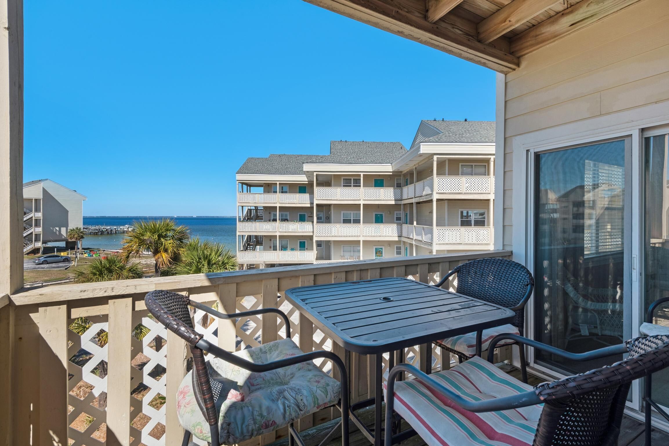 Un balcon avec une table et des chaises, donnant sur une plage et un port de plaisance.