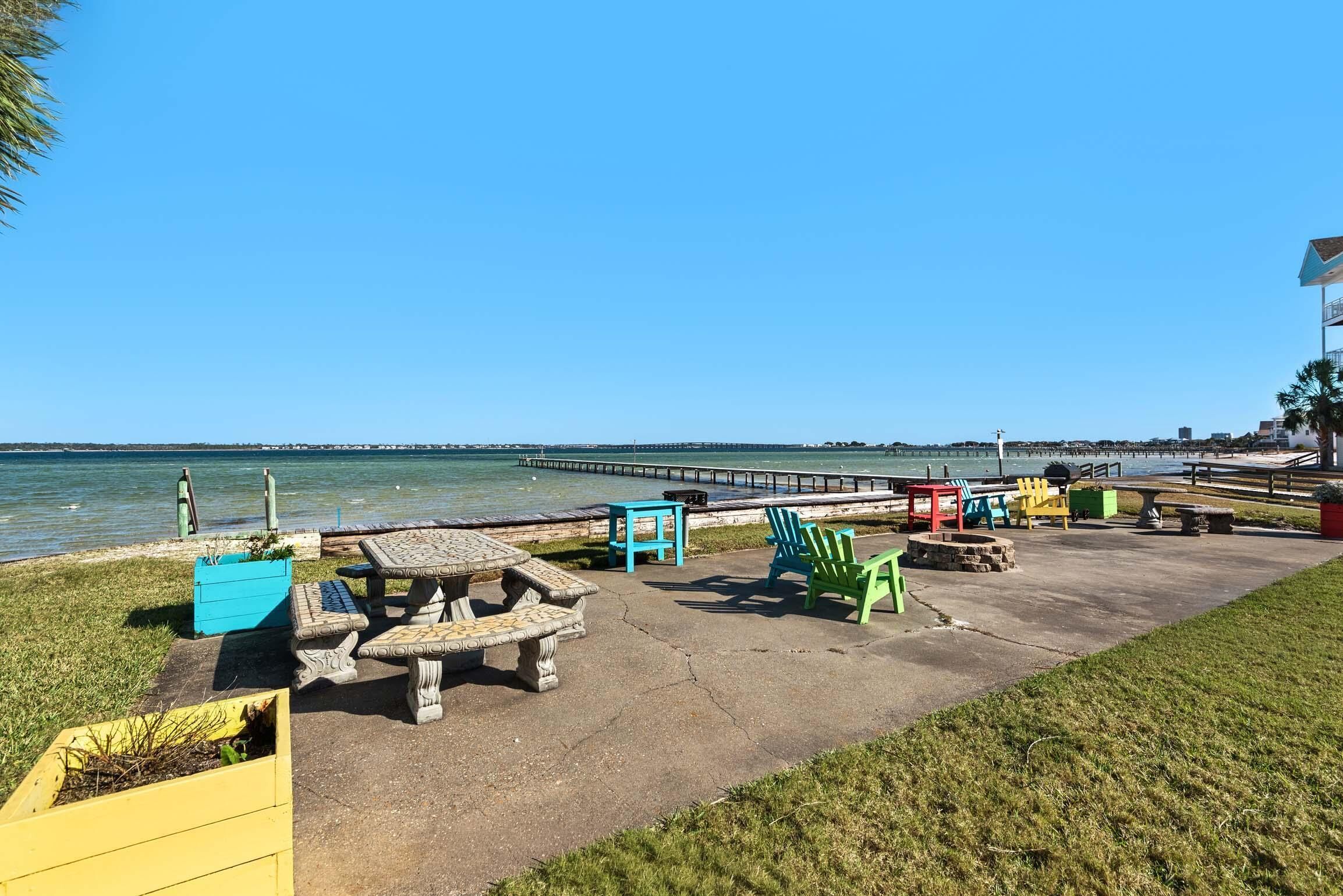 A waterfront patio with outdoor seating and a pier in the background.