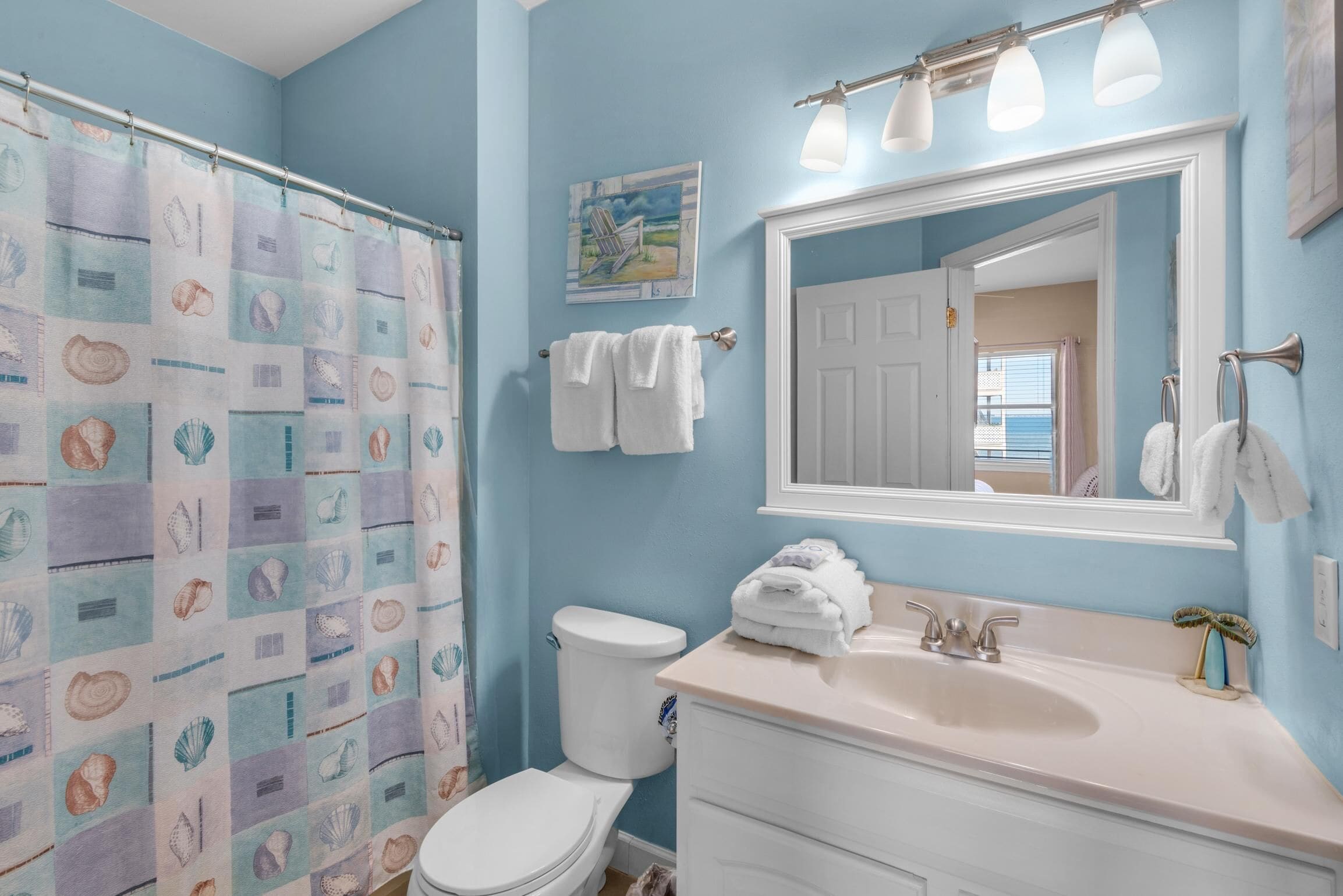 A bathroom with a blue wall, a white toilet, a sink with a mirror, and a shower curtain with a shell pattern.