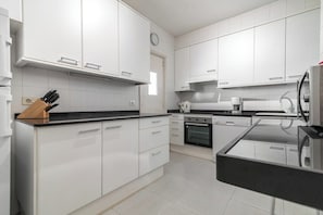 Une cuisine moderne avec des meubles blancs, un plan de travail noir et une horloge au mur.