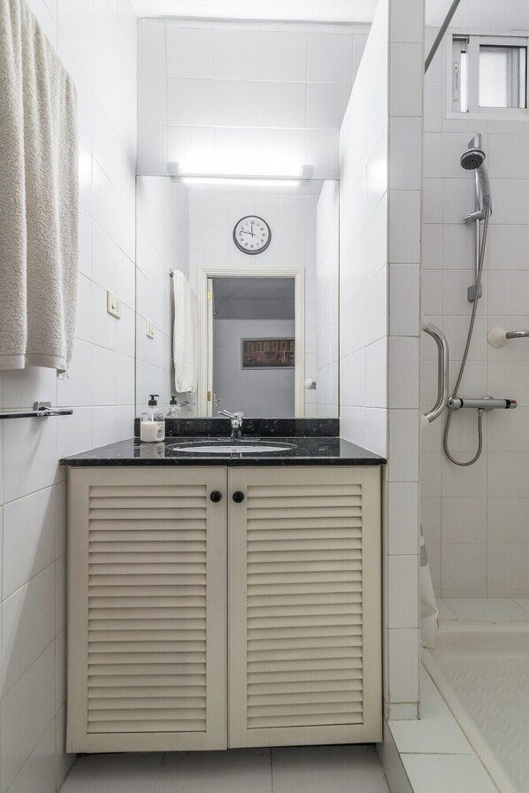 Une salle de bain équipée d’un lavabo, d’un miroir, d’une horloge, d’un porte-serviettes et d’une douche.