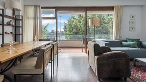 A modern living room with a wooden dining table, cushioned chairs, a sofa, and a balcony with a view of greenery. - Home2Book Bright Apt Las Palmas City Center (Las Palmas de Gran Canaria)