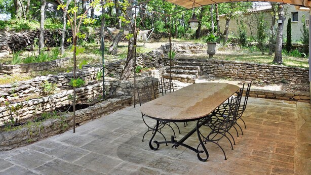 An outdoor patio with a stone table and chairs, surrounded by stone walls and greenery. - Lovely home in Lacoste (Lacoste)