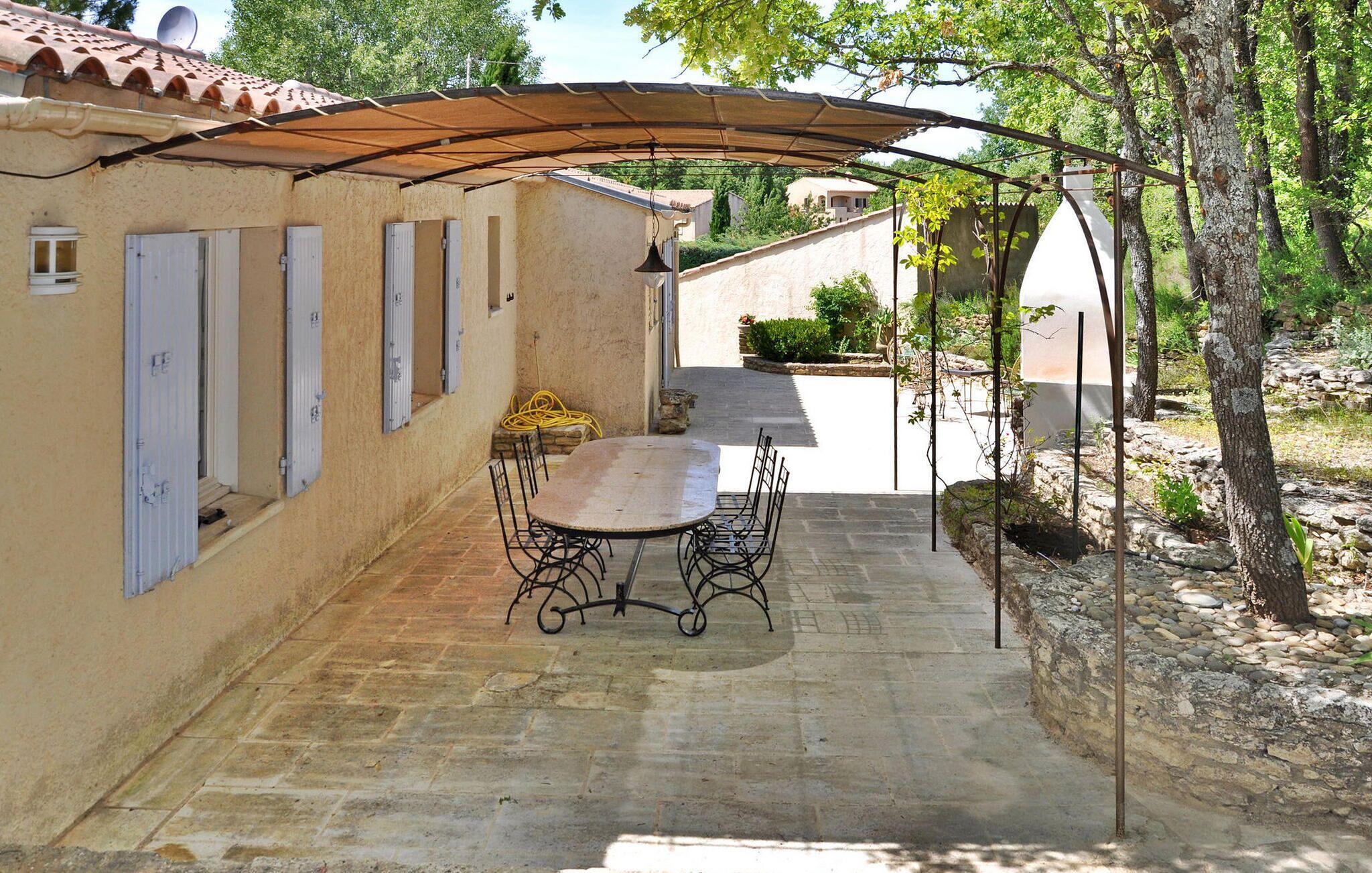 A covered patio with a table and chairs, a stone pathway, and a building with a tiled roof and windows.
