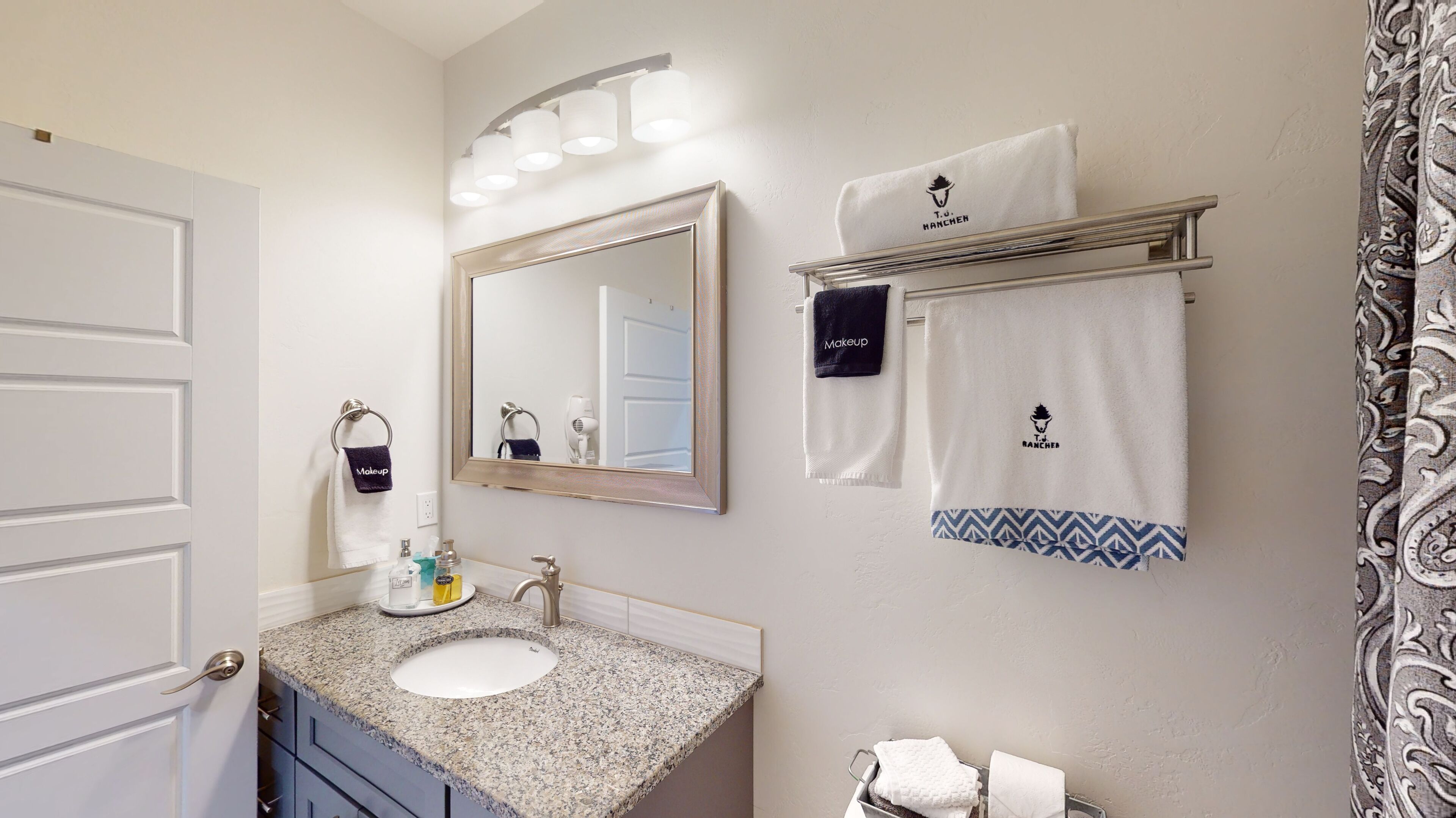 A bathroom with a granite countertop sink, a large mirror, and a towel rack with two towels.