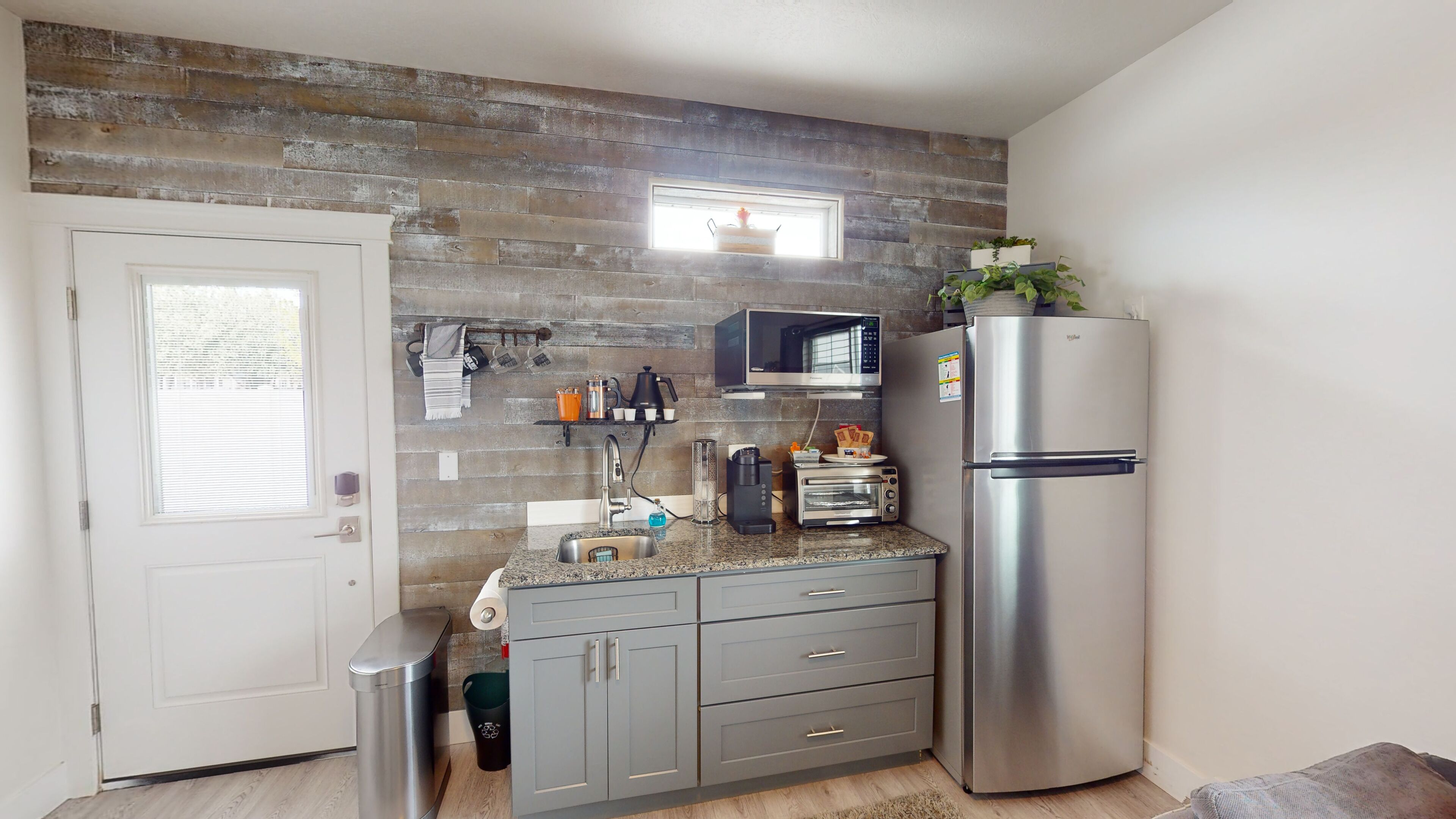 Una cocina compacta con microondas integrado, refrigerador de acero inoxidable y un ventanal sobre el fregadero.