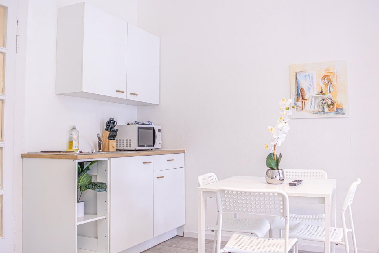 Uma cozinha compacta branca com micro-ondas, armários e uma pequena mesa com cadeiras.