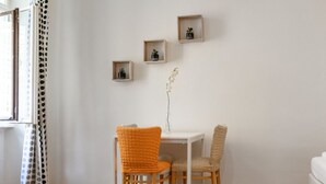 A room with a white table, two chairs, a window with a curtain, and four small wooden shelves with plants.