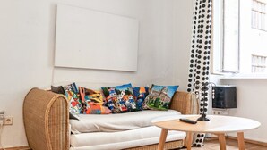 A room with a wicker sofa, a round table, a television, and a polka dot curtain.