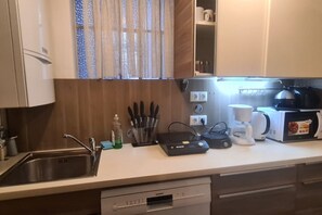 Uma cozinha com pia de aço inoxidável, cafeteira, torradeira e máquina de lavar louça.