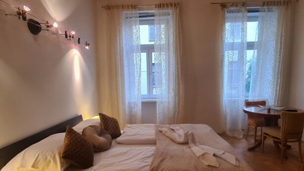 A hotel room with a bed, two windows with curtains, a table with chairs, and a wall-mounted light fixture. - Cozy City Center Retreat 2BR Apt. Homelike Comfort (Vienna)