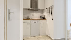 Una cocina compacta con gabinetes blancos, una campana extractora de acero inoxidable, un lavavajillas y una cafetera.