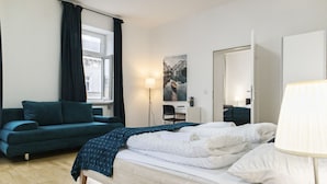 Un dormitorio con cama, sofá, escritorio, silla, lámpara y ventana.
