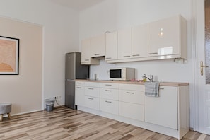 A kitchen with white cabinets, a microwave, a refrigerator, and a wooden countertop.