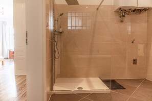 Baño con ducha envuelta en vidrio, banco, ventana y suelo de baldosas.