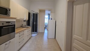 Een smalle keuken met een magnetron, oven, spoelbak en een douchecabine van glas.