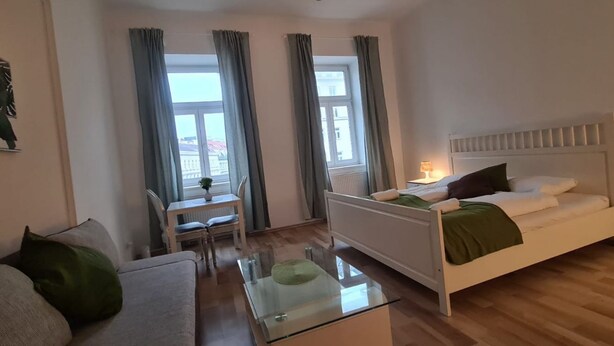 Een moderne hotelkamer met een bed, een bank, een glazen salontafel en uitzicht buiten door grote ramen.