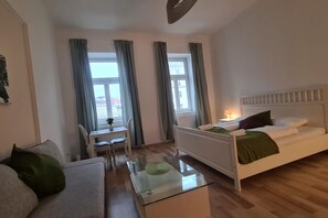 Et moderne hotelværelse med seng, sofa, sofabord i glas og udsigt til det fri gennem store vinduer.