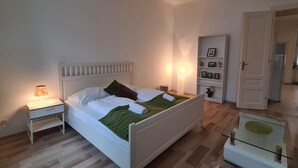 Een slaapkamer met een bed, nachtkastje, lamp en een glazen tafel met een groene tafelkleed.