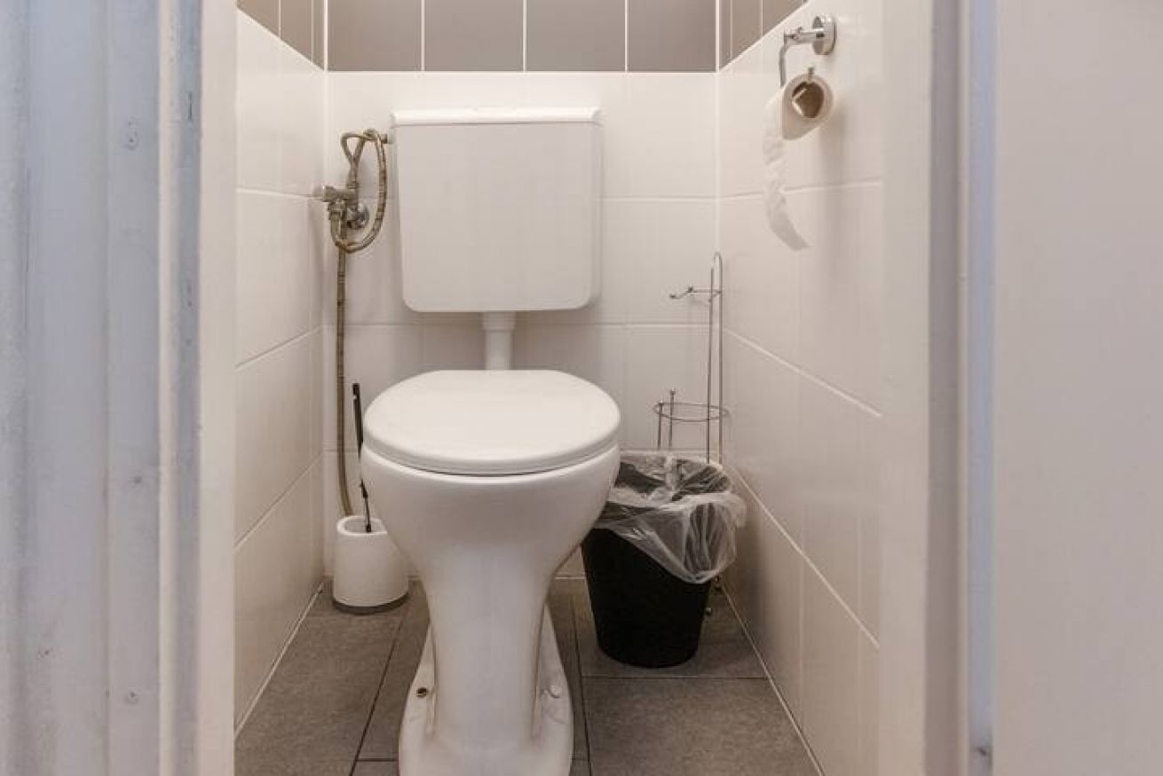 Une petite salle de bain aux murs recouverts de carreaux blancs, avec des toilettes blanches, un bidet et une poubelle.