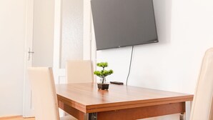 A conference room with a wooden table, two chairs, a potted plant, and a mounted flat-screen TV. - Cheerful 2BR Apartment - Suitable for Longstays (Vienna)