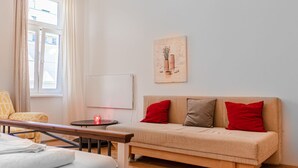 A room with a sofa, a table, a bed, a window with curtains, and a wall-mounted artwork. - Cheerful 2BR Apartment - Suitable for Longstays (Vienna)