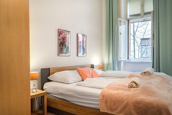 A hotel room with a wooden bed, two pillows, a bedside table with a lamp, and two wall art pieces.