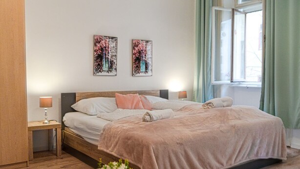 Une chambre à coucher avec un lit en bois, deux tables de chevet, une fenêtre avec des rideaux et deux œuvres d’art accrochées au mur.