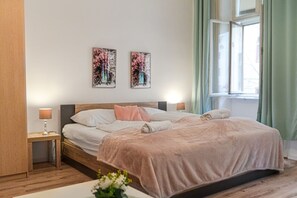 Un dormitorio con una cama de madera, dos mesitas de noche, un ventanal con cortinas y dos obras de arte colgadas en la pared.