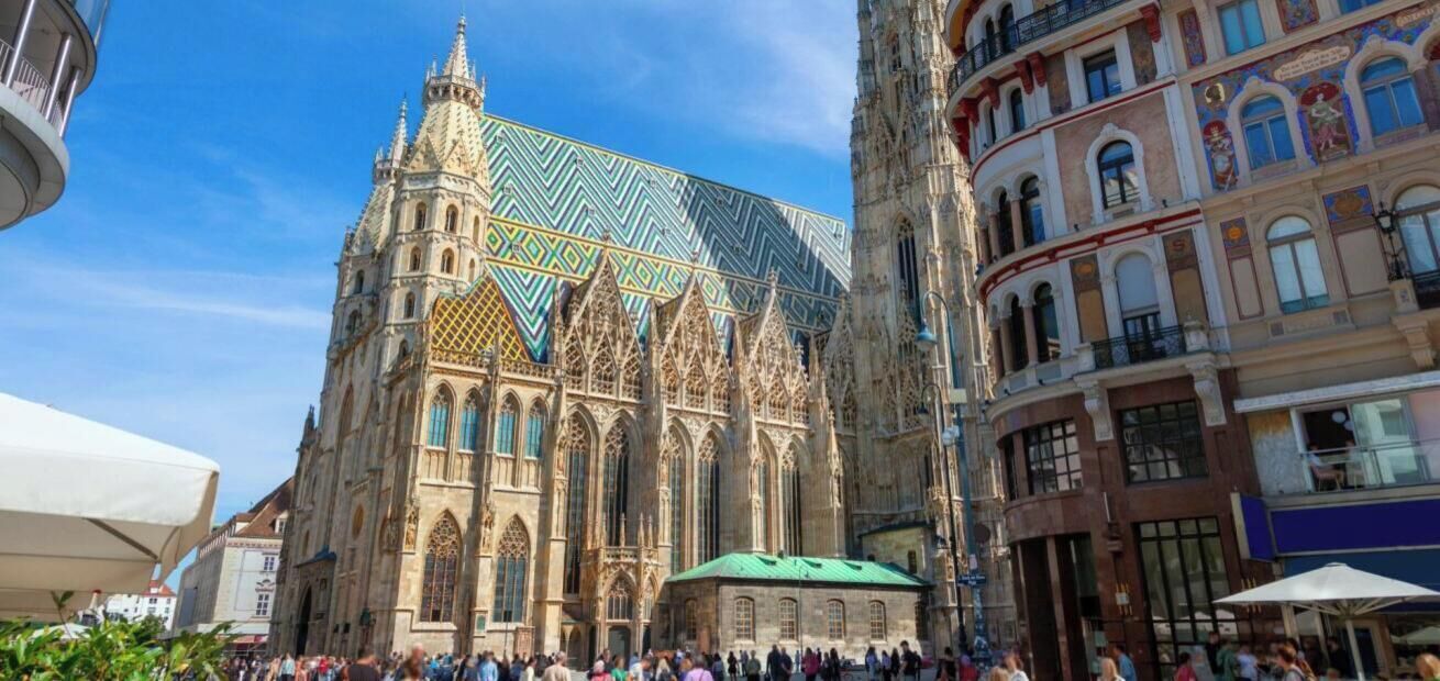 A historic cathedral with Gothic architecture, a large crowd, and adjacent modern buildings.