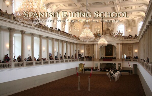 Un gran salón con techos altos, candelabros ornamentados y una zona central con caballos.