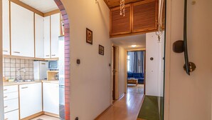 A narrow hallway with a kitchen on one side, wooden ceiling, and a blue sofa in the background. - Vienna's Finest: Spacious Apt. w/2+1 Configuration (Vienna)