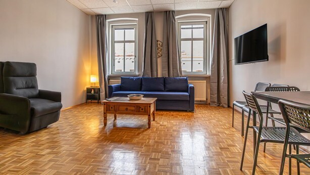 A living room with a sofa, a coffee table, a TV, and a dining area with chairs. - Vienna's Finest: Spacious Apt. w/2+1 Configuration (Vienna)