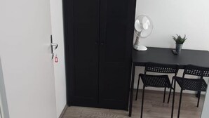 A room with a black door, a white wall, a small table with a fan, two black chairs, and a potted plant. - Enkplatz U3 Getaway: Affordable 5-BR Apartment (Vienna)