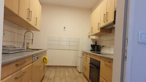 A compact kitchen with wooden cabinets, a white tiled backsplash, a refrigerator, and a dishwasher. - Relaxing 2-Bed Apartment for Extended Visits (Vienna)