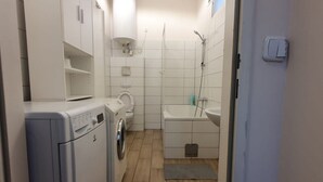 A compact bathroom with a washing machine, toilet, and shower area. - Relaxing 2-Bed Apartment for Extended Visits (Vienna)