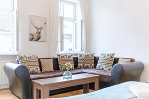 A modern living room with a brown leather sofa, patterned cushions, a wooden coffee table with a vase, and a deer painting on the wall.