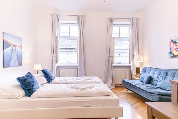 A bedroom with two beds, a sofa, a lamp, and a painting on the wall.