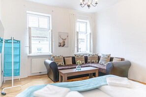 A room with a sofa, a coffee table, a radiator, and a window with curtains.