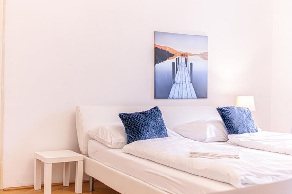 A bedroom with a bed, pillows, a bedside table, and a wall-mounted picture.