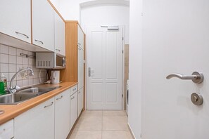 Une cuisine étroite avec des meubles blancs, un four à micro-ondes, un évier et une porte donnant sur une autre pièce.