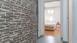 Ein Korridor mit Backsteinwand, der zu einem Schlafzimmer mit Bett und Nachttisch führt.