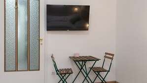 Ein Zimmer mit einer Schiebetür aus Glas, einem Wand-Fernseher und einem kleinen Holztisch mit zwei Stühlen.