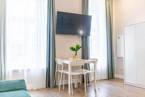 A room with a TV mounted on the wall, a dining table with chairs, a potted plant, and a wardrobe.