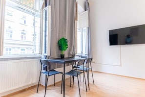 A room with a table and chairs, a potted plant, a window with curtains, and a mounted TV.