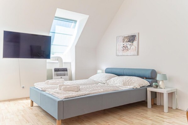 A modern bedroom with a bed, a TV mounted on the wall, a small bedside table, and a window.