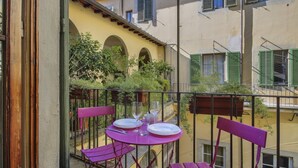 A balcony with a table set for two, surrounded by chairs, overlooking a courtyard with arches and greenery. - Lemon Tree One Bedroom with Balcony (Florence)