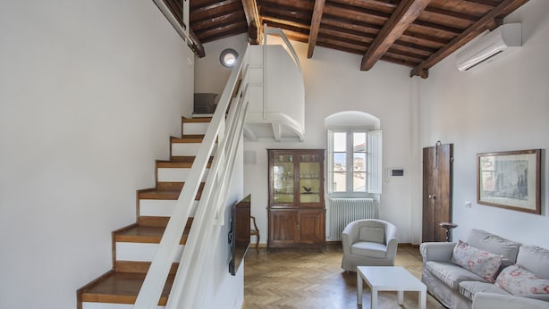 A spacious living area with a wooden staircase, a white sofa, and a dining table. - Maggio In Florence (Firenze)