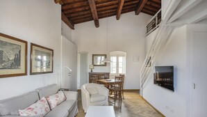 A living room with a sofa, a dining table with chairs, a TV mounted on the wall, and a staircase leading to an upper floor. - Maggio In Florence (Firenze)